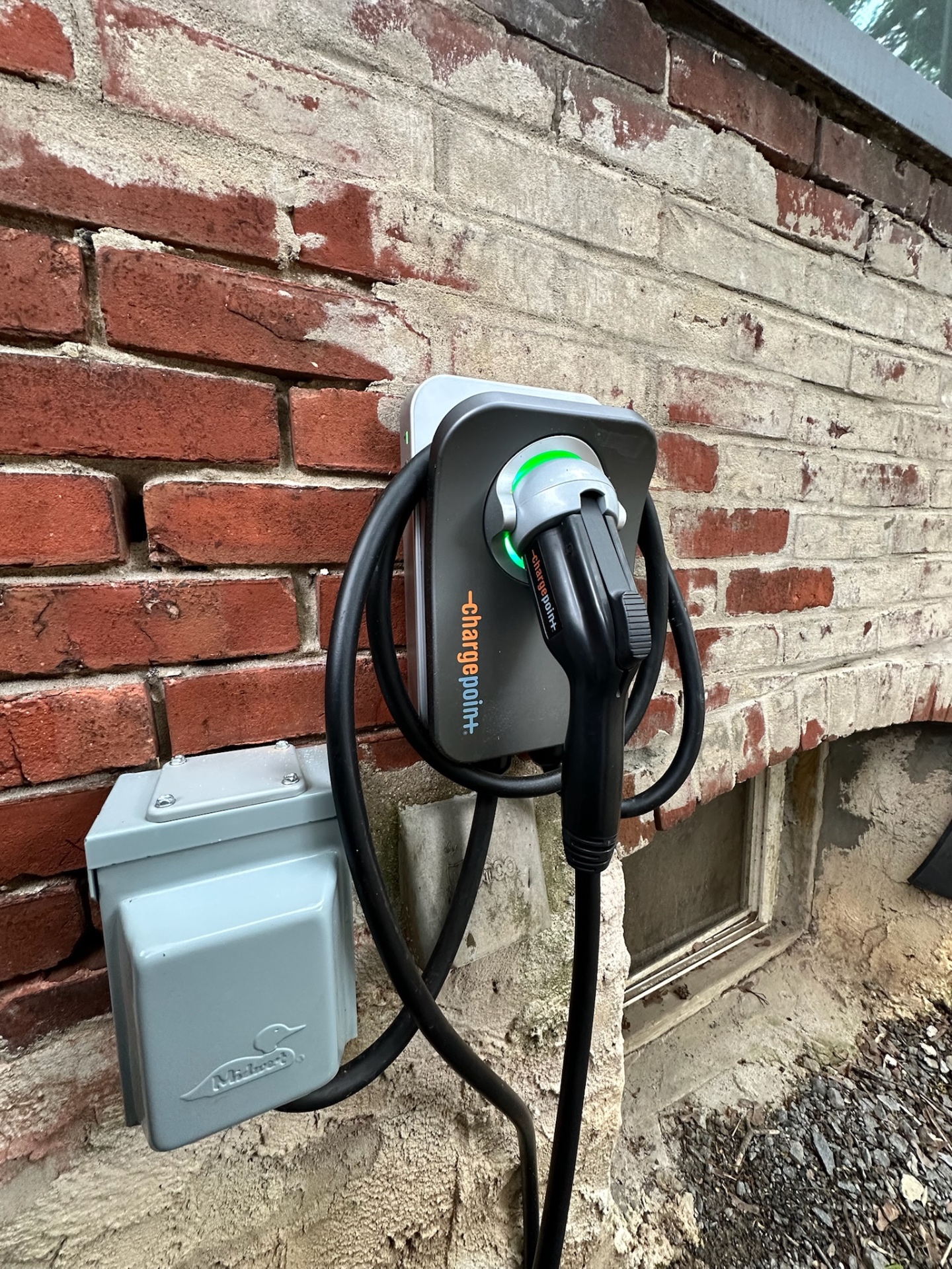 ChargePoint EV charger mounted on a brick wall with a weatherproof disconnect box for safe outdoor installation