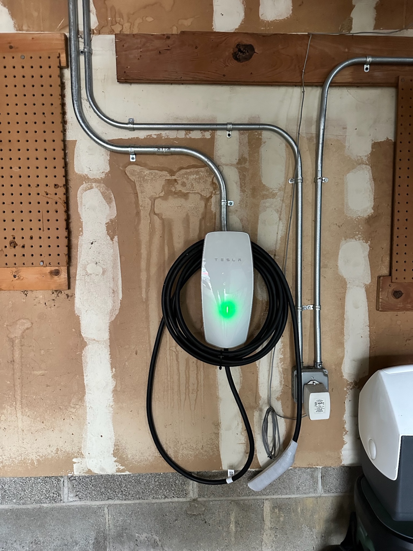 Tesla Wall Connector installed in a garage with multiple rigid metal conduit runs to the electrical panel